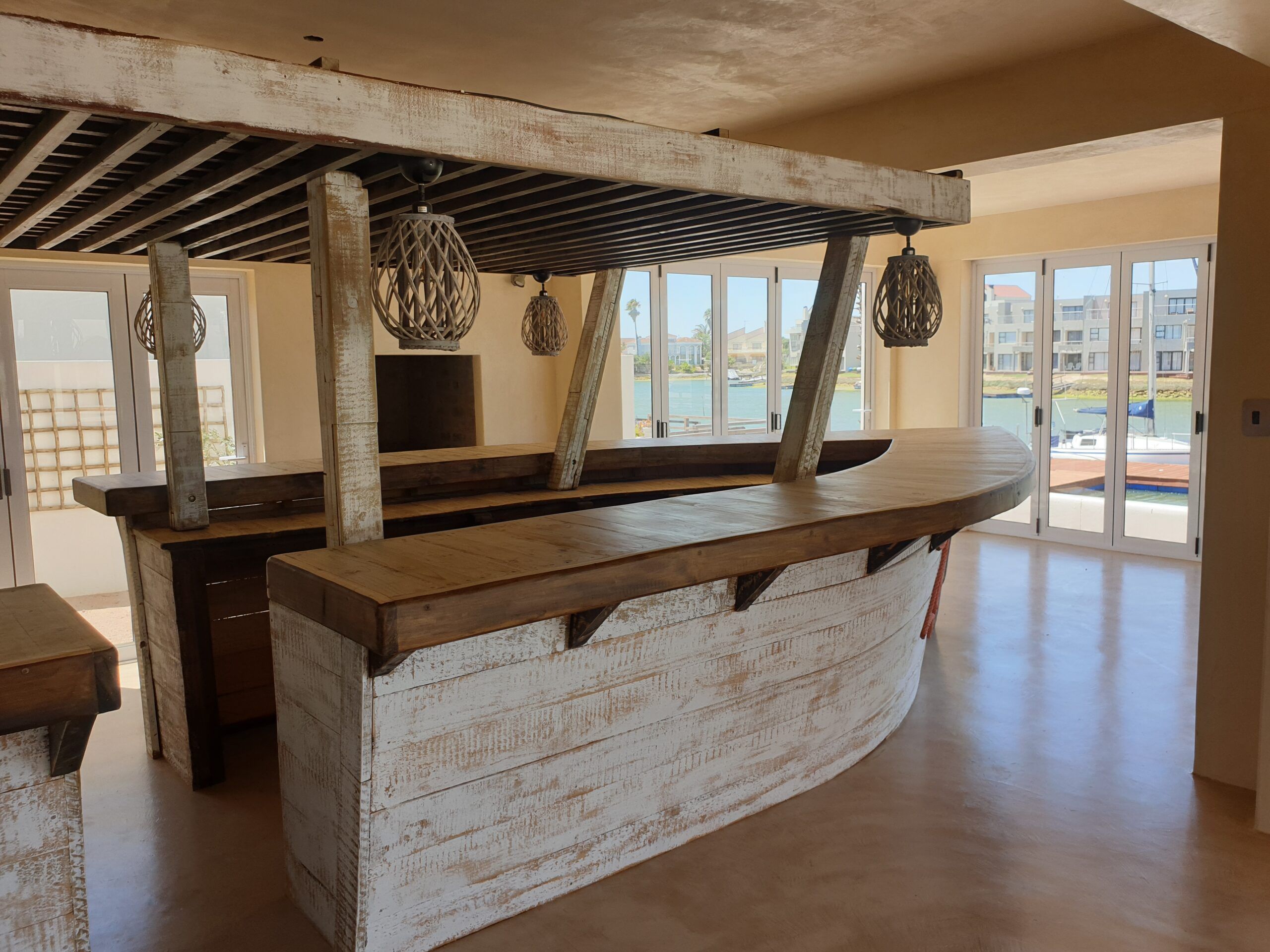 Sand-coloured cement screed floor beside a whitewashed timber bar with wicker pendant lights