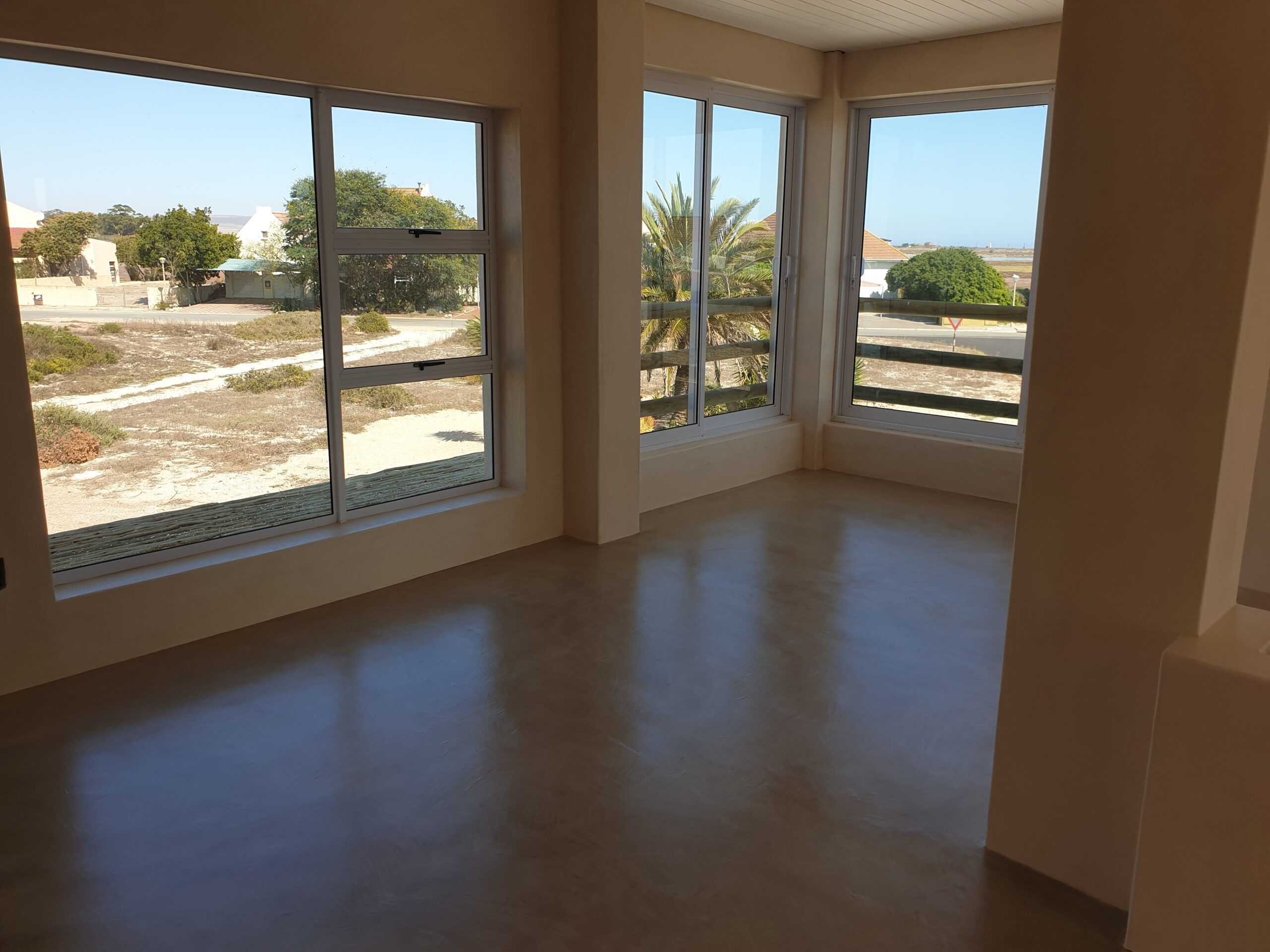 Grey-brown cement screed floor in a bright corner room with large aluminium windows