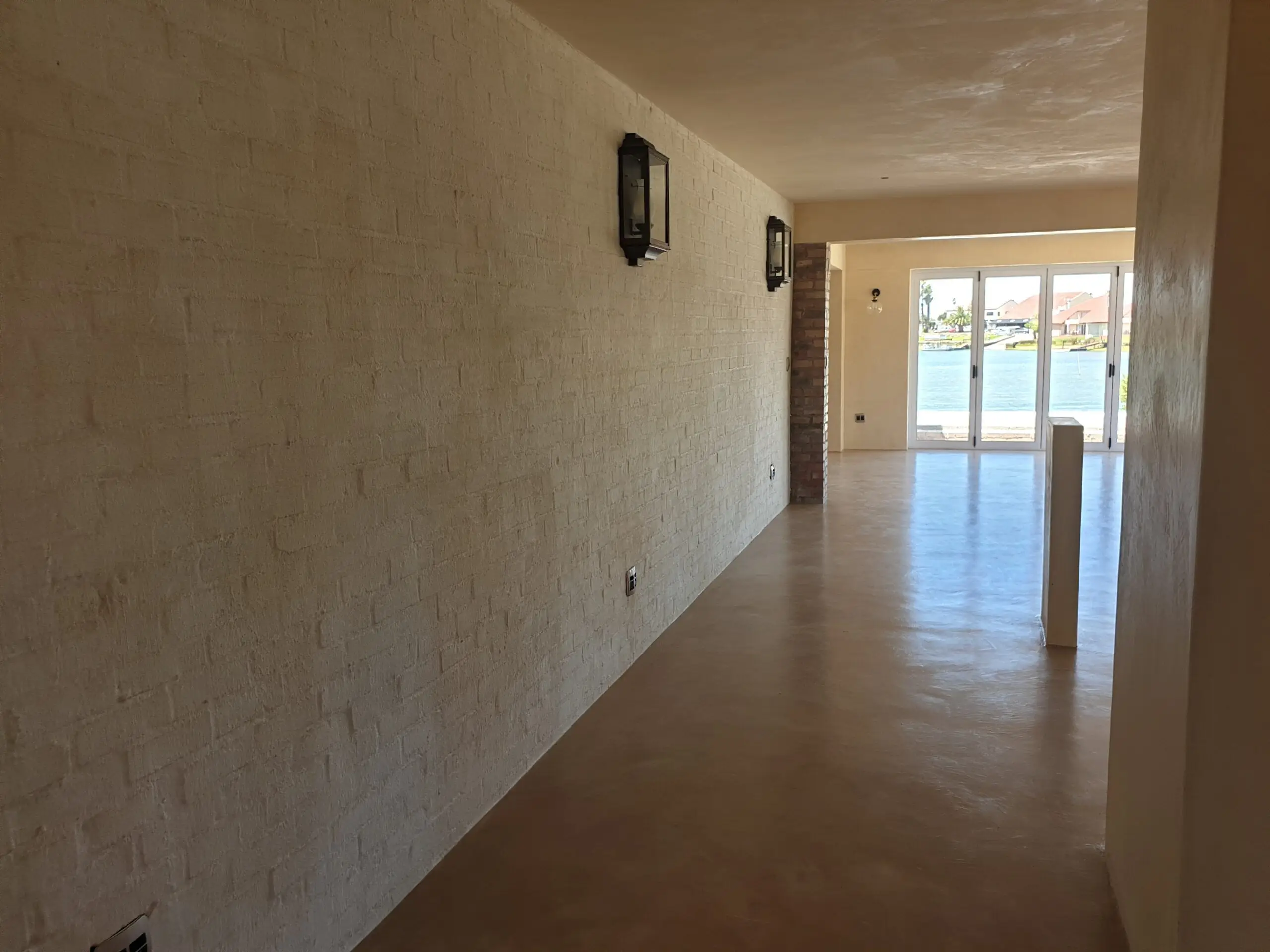 Warm sand-coloured cement screed floor in a long passage with whitewashed brick wall and lanterns