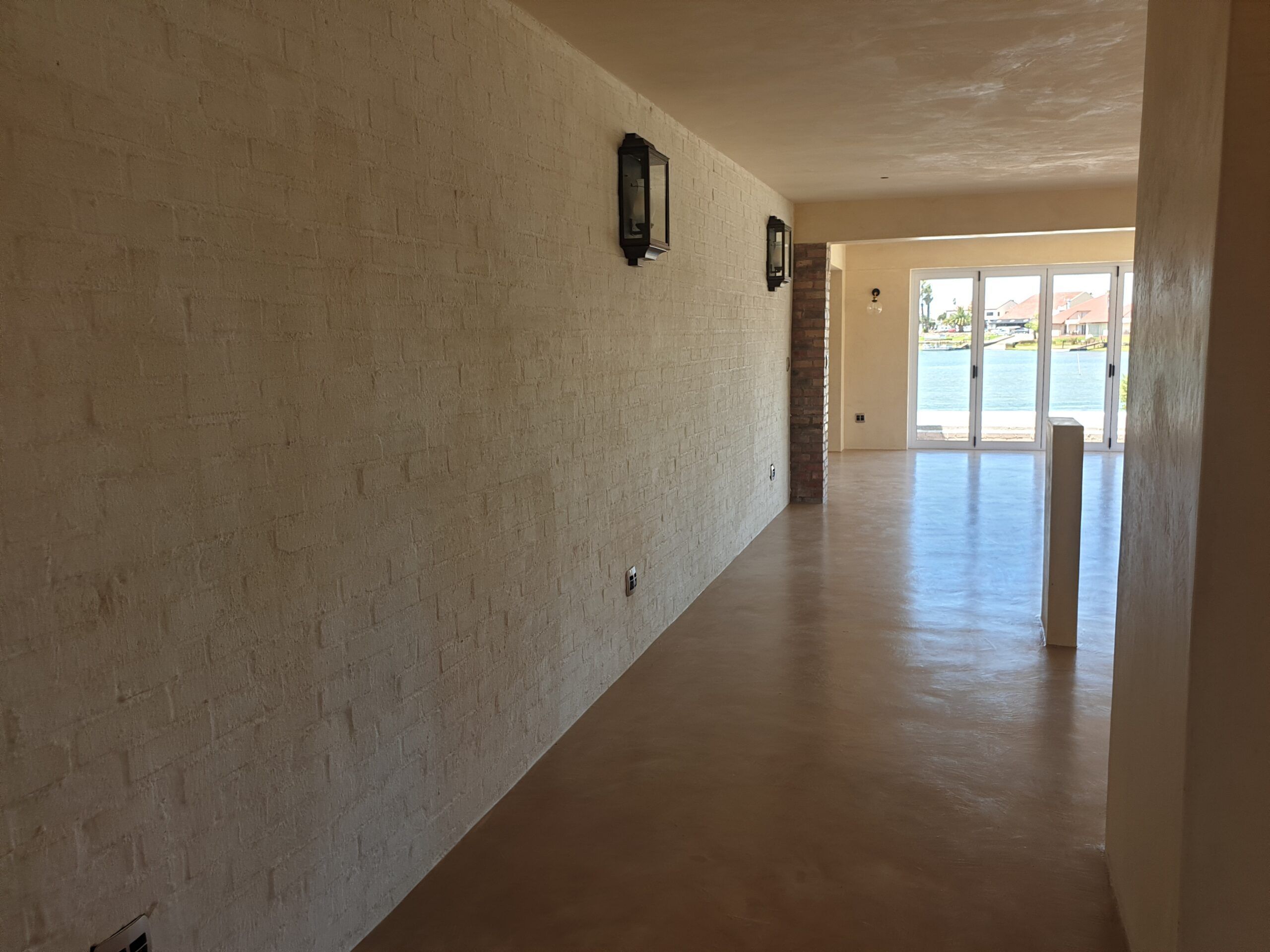 Warm sand-coloured cement screed floor in a long passage with whitewashed brick wall and lanterns