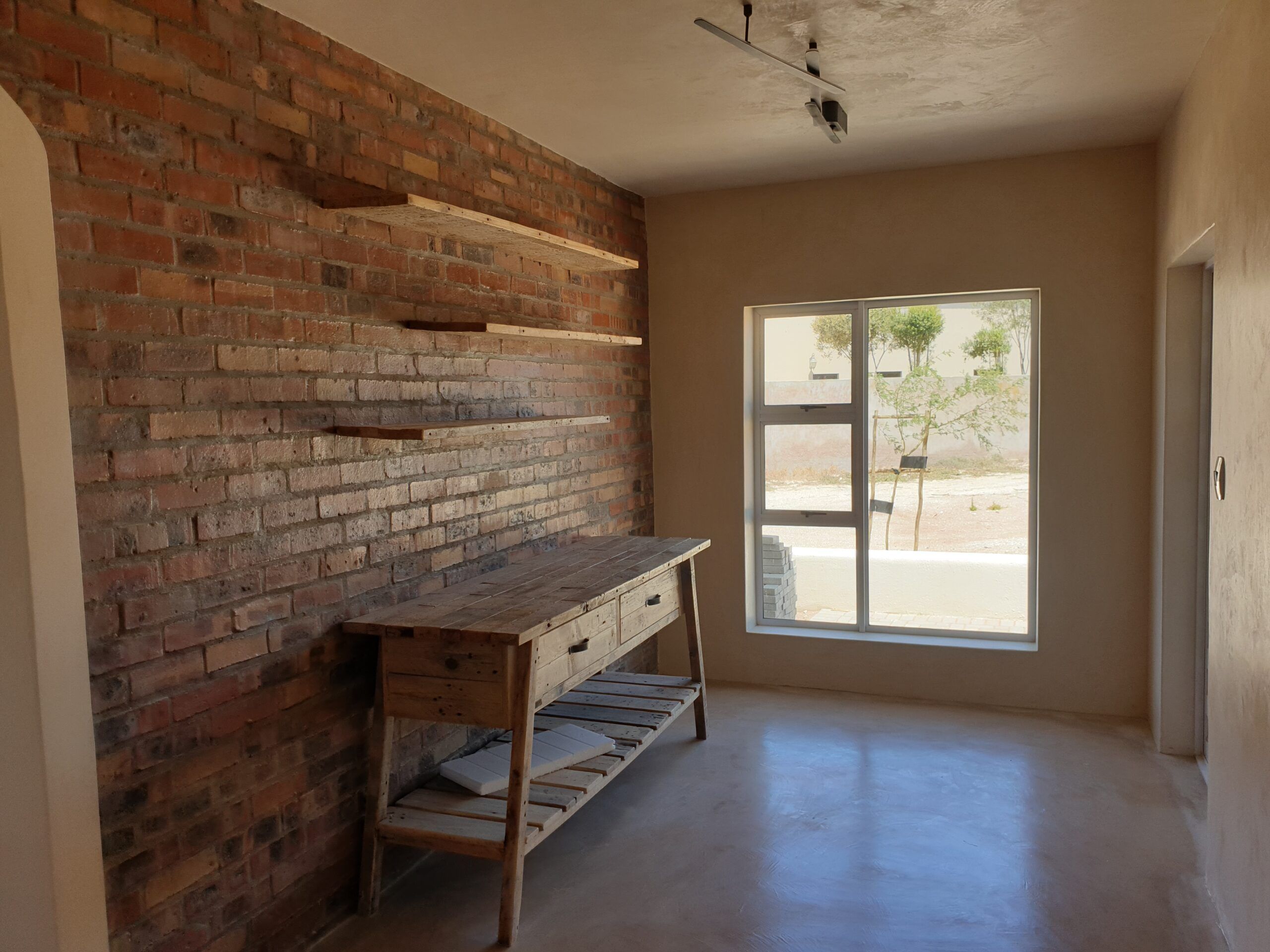 Pale grey cement screed floor in a room with exposed face-brick wall and reclaimed-wood console
