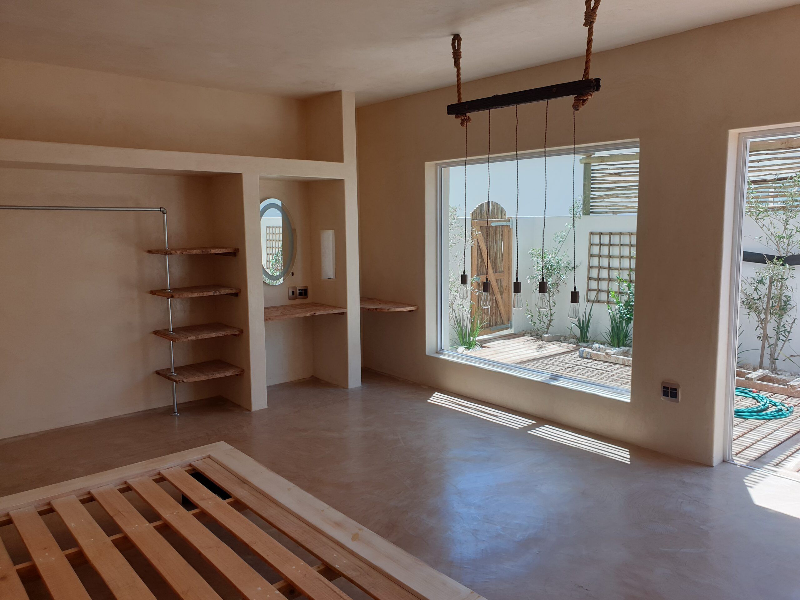 Bedroom with cement screed floor, built-in screed niches, timber shelves and rope pendant light
