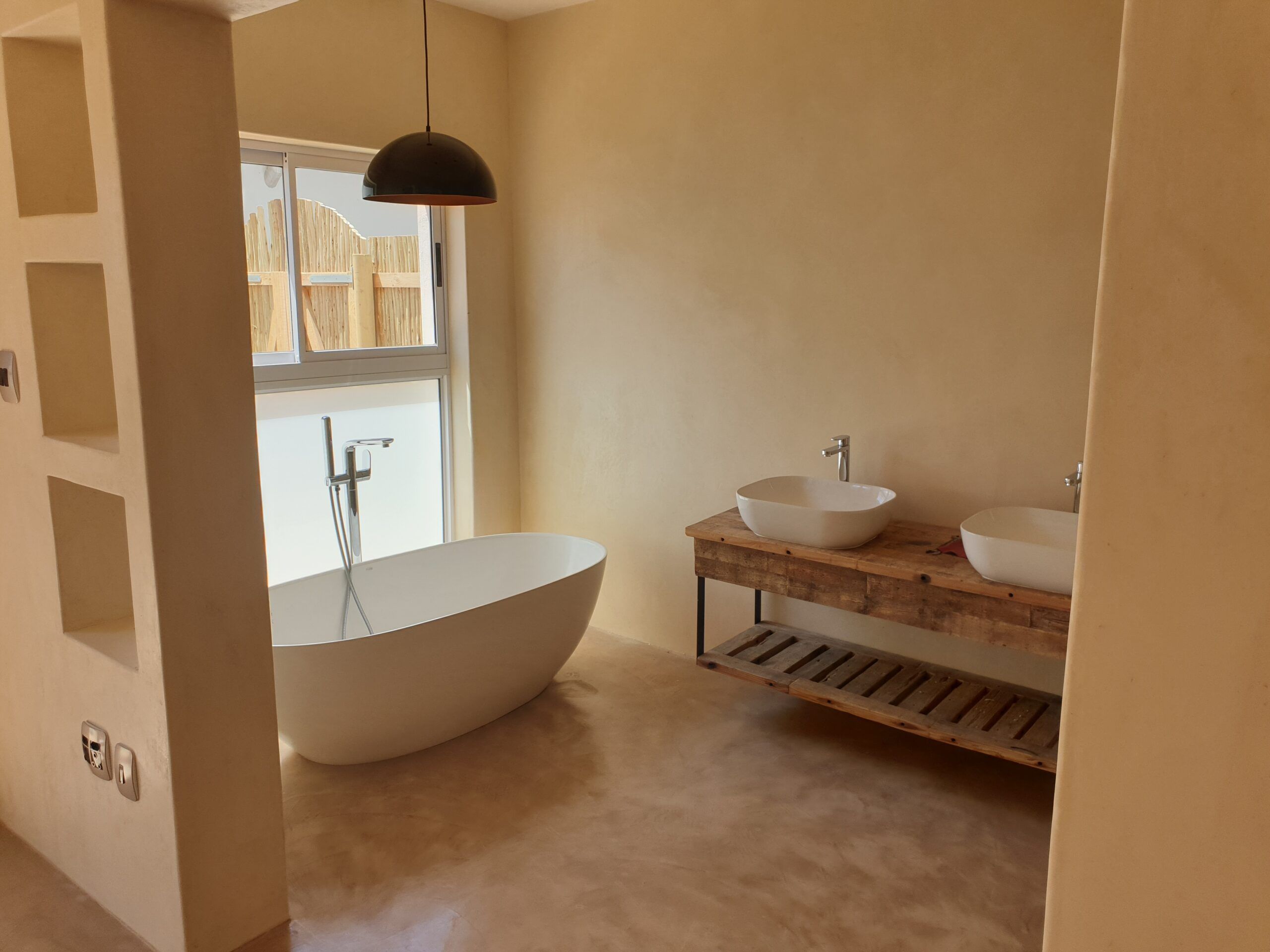 Freestanding white bath on a warm cement screed floor with matching walls and wall niches