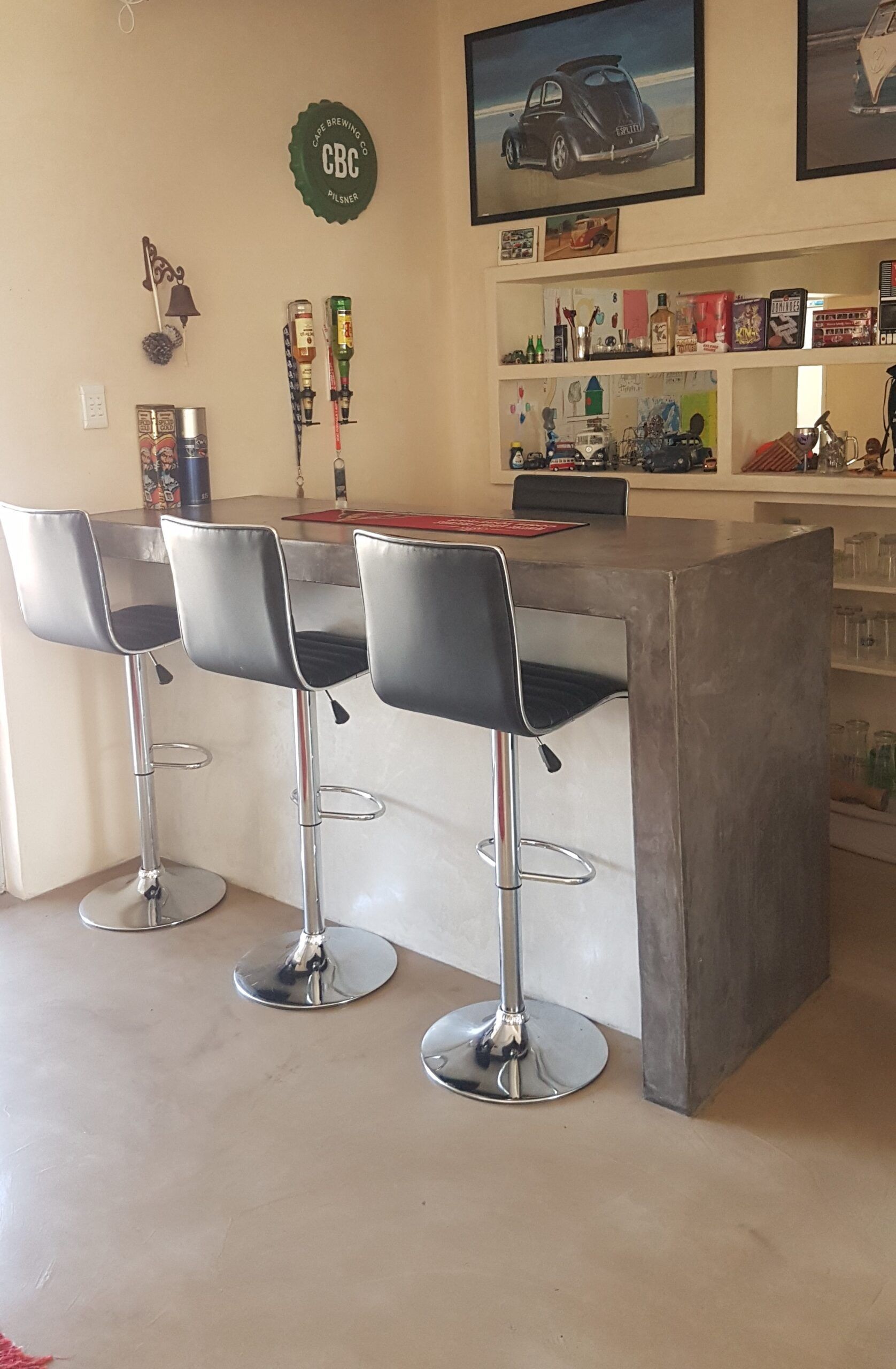 Grey cement screed bar counter with waterfall edge, black bar stools and matching screed floor