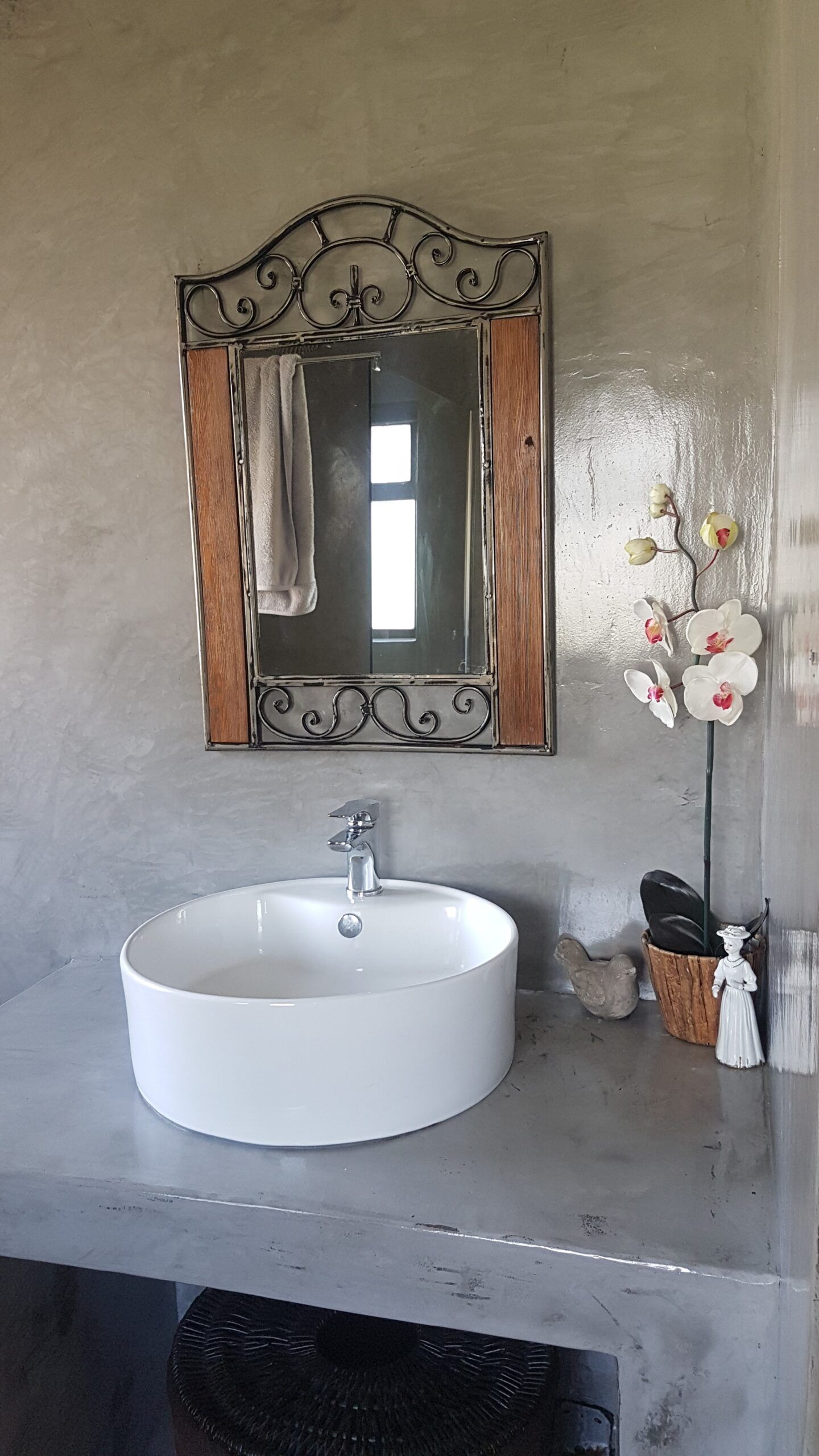 Grey cement screed vanity top and wall with a round white basin and iron-framed mirror