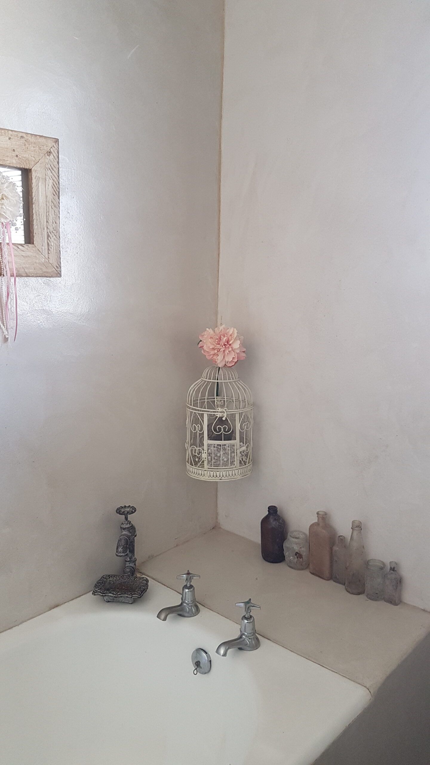Pale cement screed bath surround and walls with chrome cross-head taps and vintage bottles